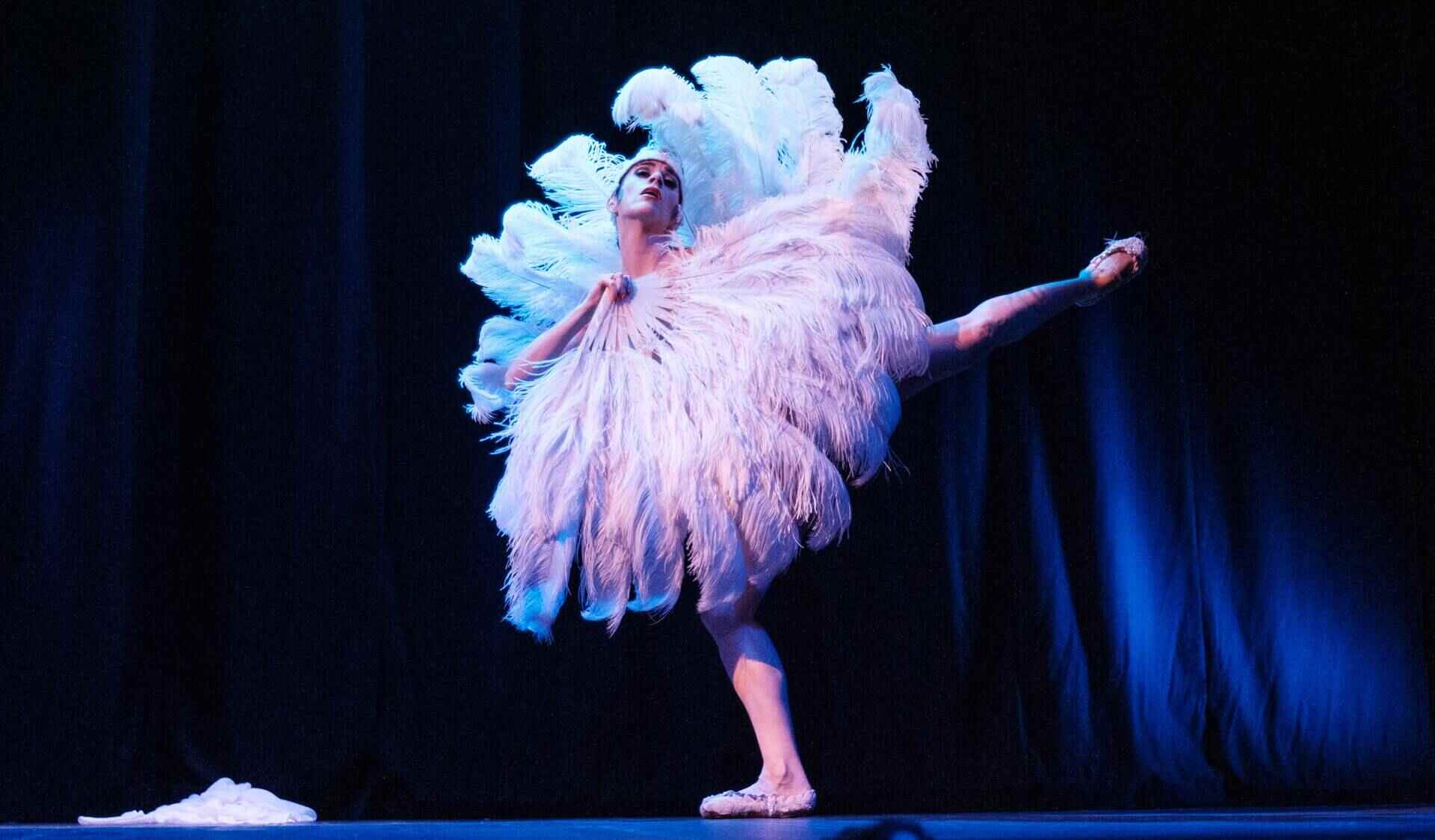 Ballerina with feather fans and point shoes dancing in a black box theater